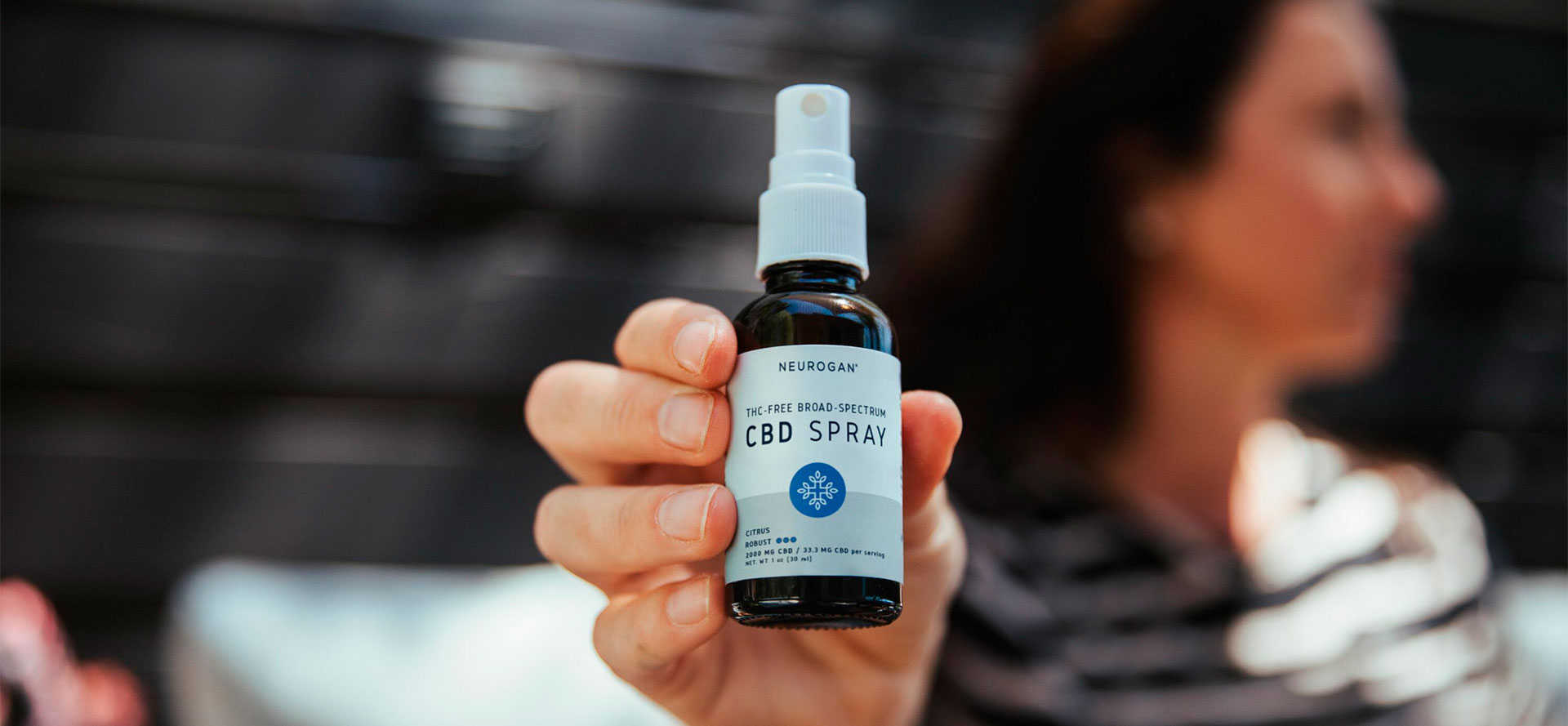 Woman showing Broad-Spectrum CBD bottle.